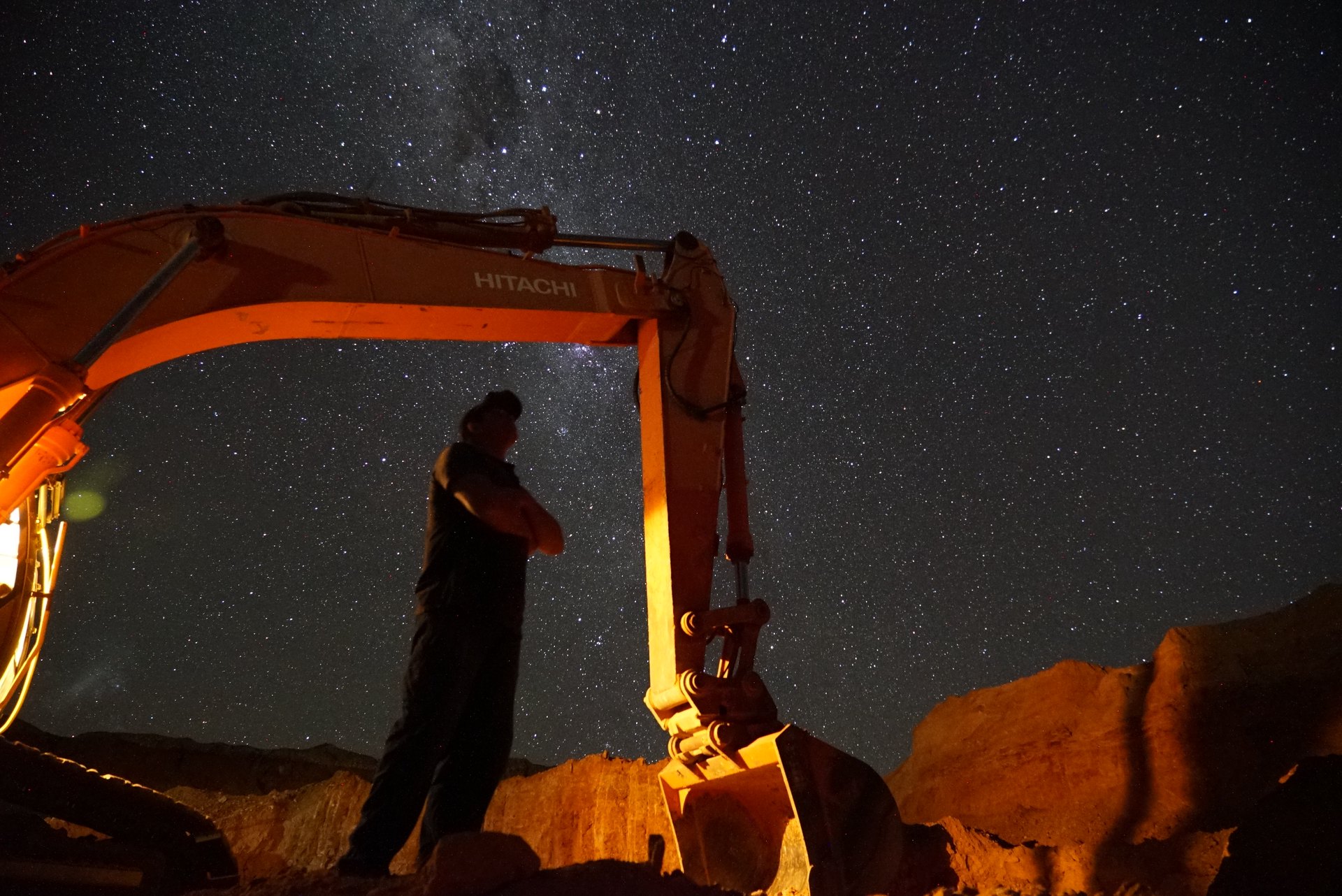 Dan standing beneath an excavator boom under the Milky Way.
