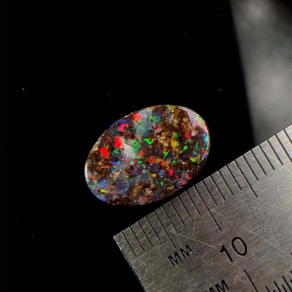 Boulder opal with red, green and blue colour beside a ruler.