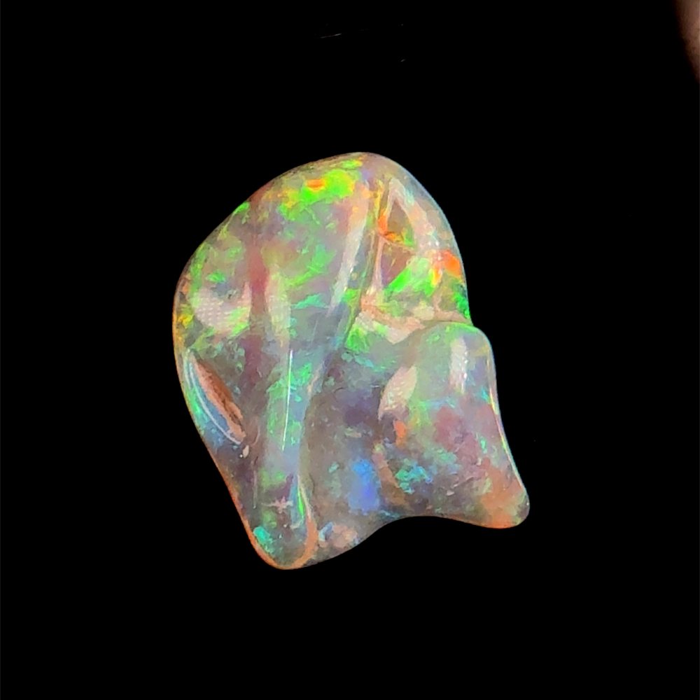 A carved freeform opal with green, orange and red colour.