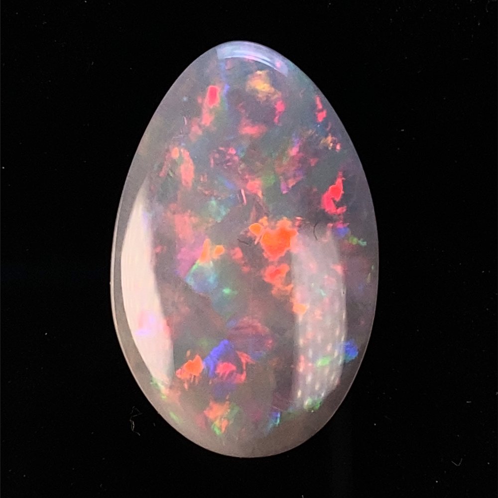 A polished teardrop opal showing pink, red and orange colour.