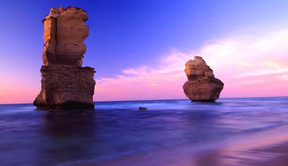 Two limestone sea stacks standing in the surf at dusk.