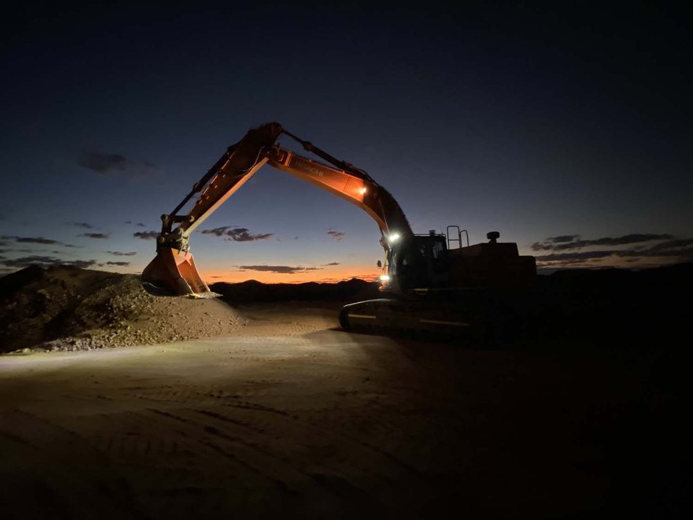 An excavator silhouetted over a spoil heap at dusk.