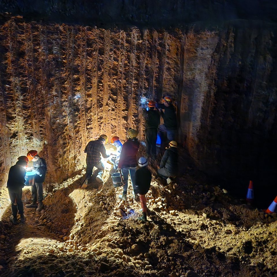 Guests in headlamps working at a lit mine face at night.