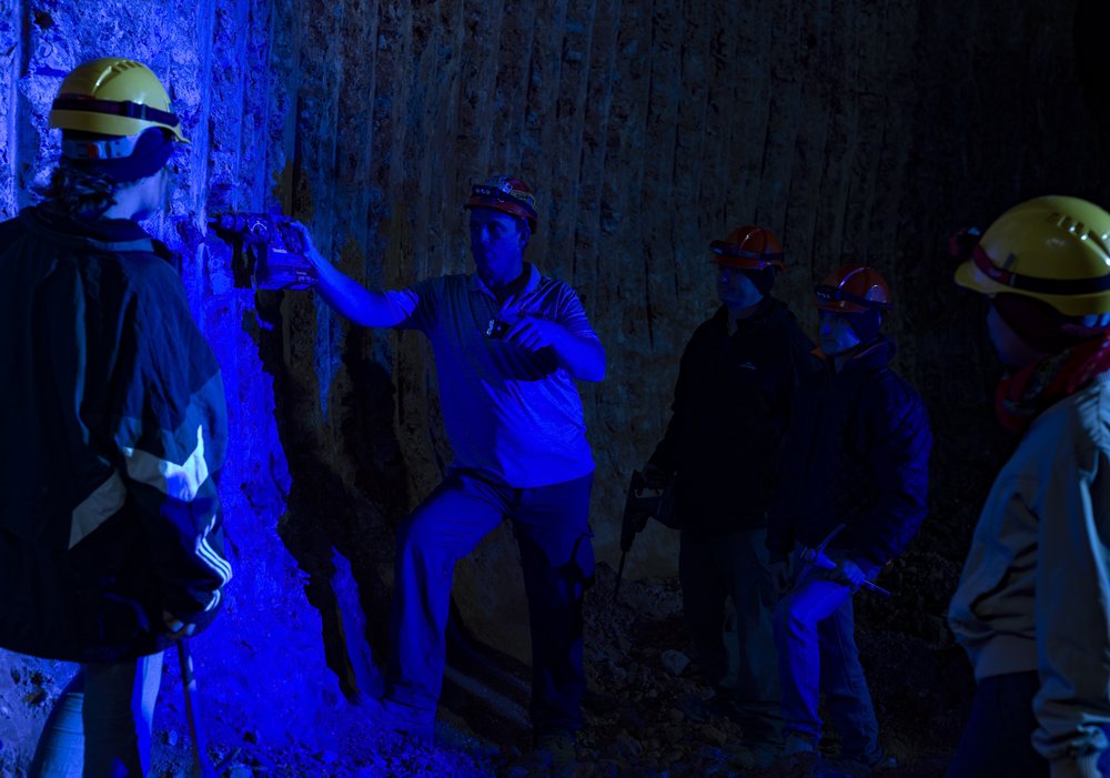 Helmeted guests searching an underground seam under ultraviolet torchlight.